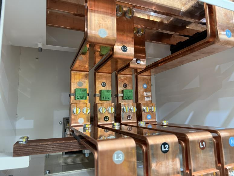 Close-up of copper busbars inside an electrical panel, labeled L1, L2, L3, and N, with green circuit components and visible bolts securing the connections.