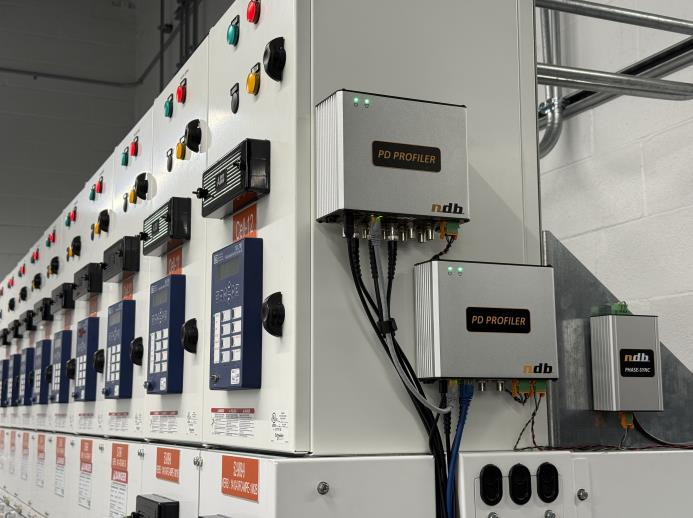 A close-up view of electrical control panels with multiple switches, buttons, and digital displays. Two metal boxes labeled PD Profiler are mounted on the side, with cables connected to them.